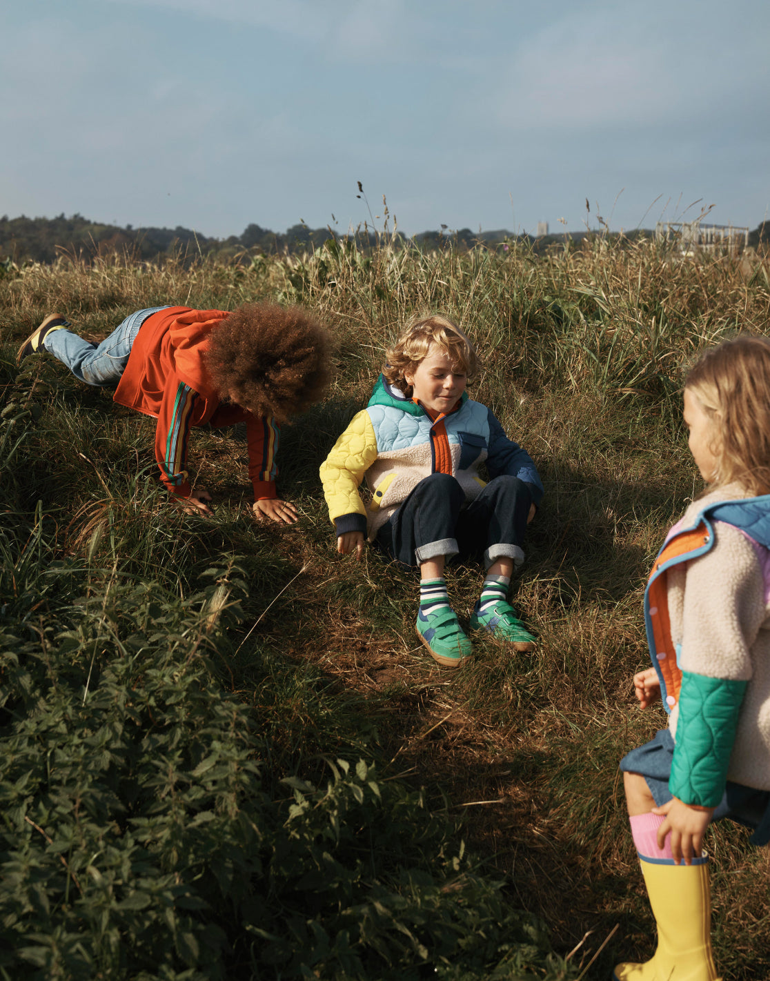 Three children playing in a field wearing Boden outerwear. 