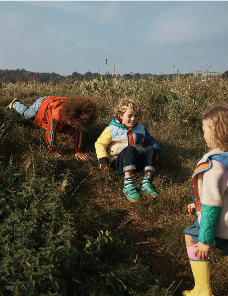 Three children playing in a field wearing Boden outerwear. 