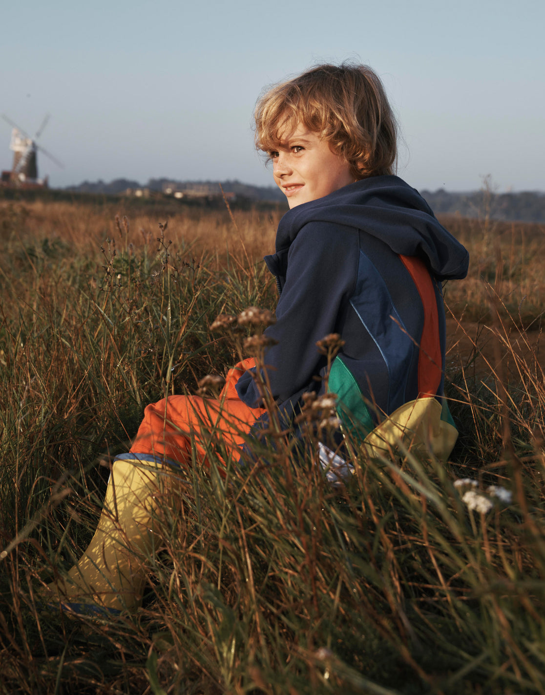 Boy sat in a field wearing a Boden hoodie.