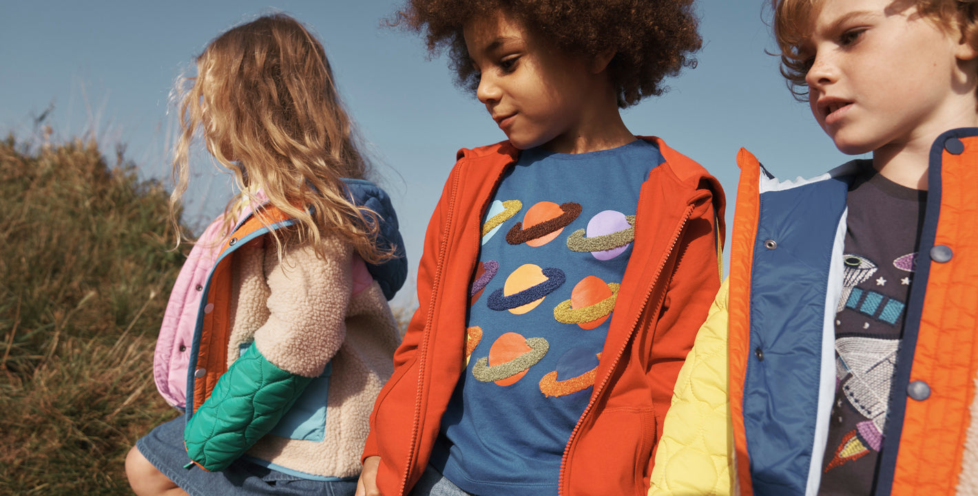 A girl and two boys walking in a field wearing Boden clothing