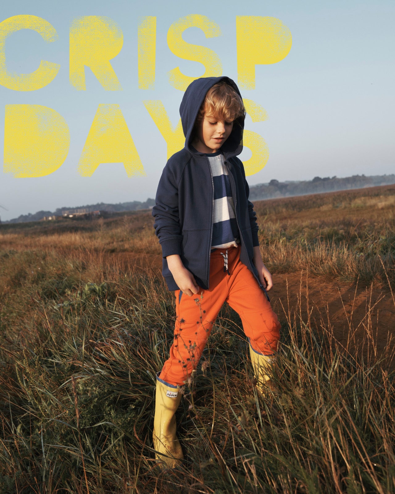 Boy standing in a field wearing Boden hoodie, Sweatpants and Wellies.