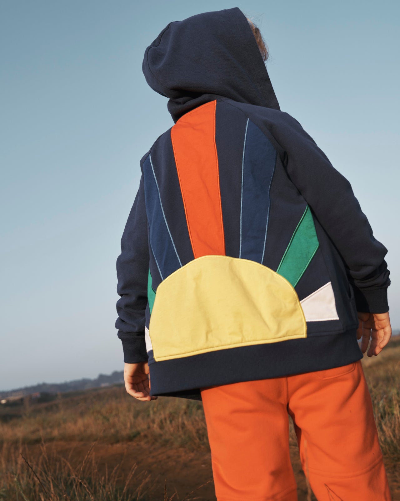 Boy with his back to the camera wearing a Boden hoodie with a sun on the back.