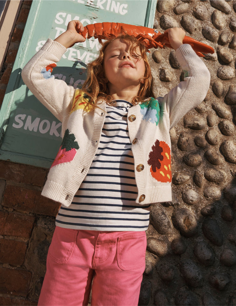 Girl holding a plastic lobster wearing a Boden knit cardigan with a colorful strawberry design.