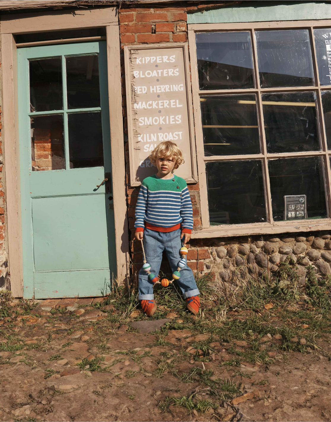 Boy leaning against a shop front wearing a striped Boden sweater.