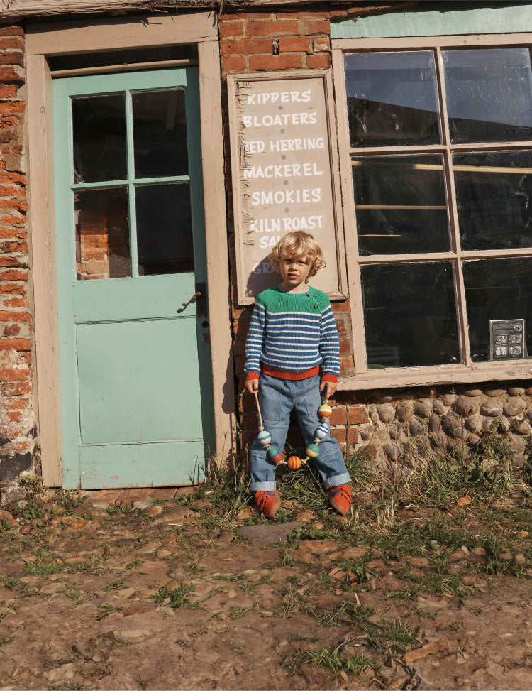 Boy leaning against a shop front wearing a striped Boden sweater.